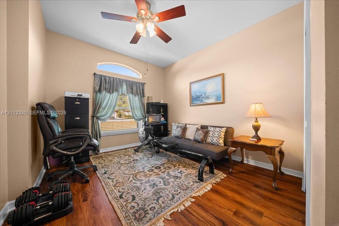 Room featuring wood-finish flooring, vaulted ceiling, ceiling fan with integrated lighting, and an arched transom window