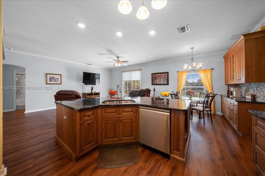 Kitchen featuring wood cabinetry, dark stone-surfaced countertops, a center island with an integrated stainless steel dishwasher, wood-finish flooring, and recessed ceiling lighting