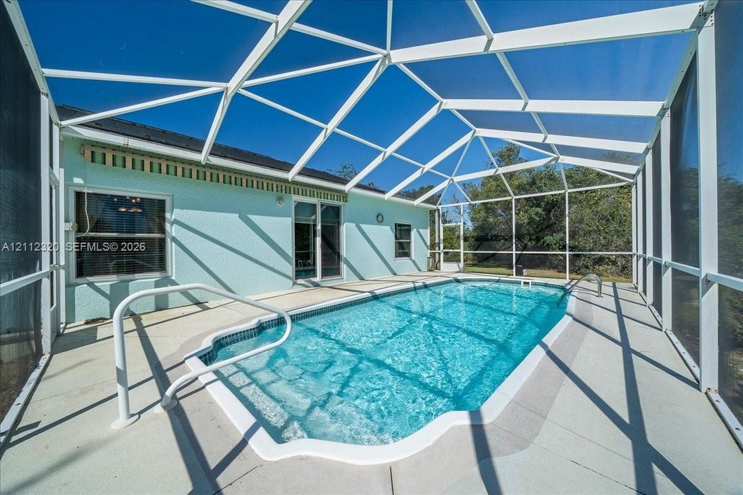 Screened-in patio area featuring a swimming pool, concrete decking, metal pool handrails, and a protective pool cage