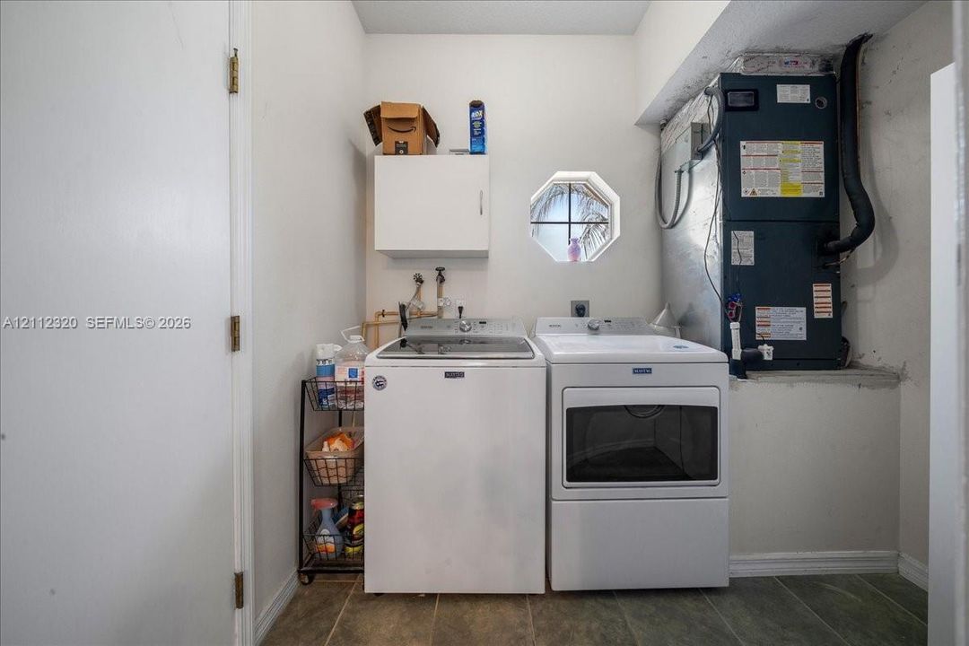 Utility area featuring ceramic tile flooring, an octagonal window, and white wall-mounted cabinetry