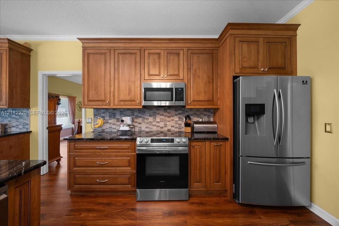 Kitchen featuring wood cabinetry, stainless steel appliances, dark countertops, a mosaic tile backsplash, and wood-finish flooring