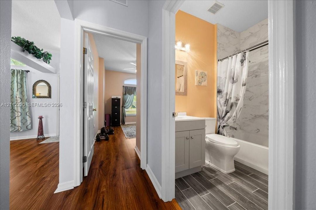 Bathroom featuring a stone-finish tub surround, wood-finish floor planks, and a shaker-style vanity with a solid-surface countertop