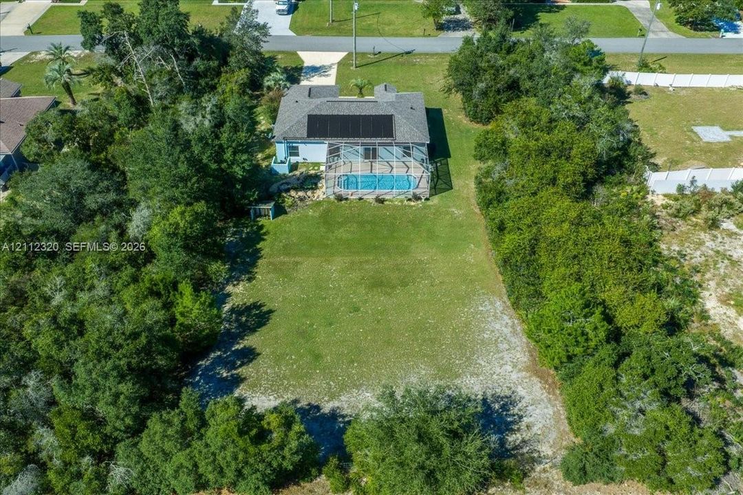 Aerial perspective featuring a large lot with extensive mature landscaping, a screened-in swimming pool, and roof-mounted solar panels