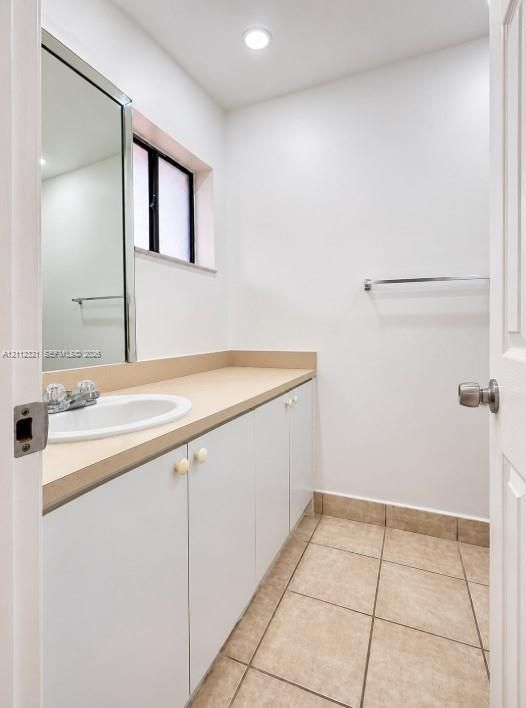 Bathroom featuring a white vanity with a neutral solid-surface countertop, an integrated drop-in sink, recessed lighting, and tile flooring