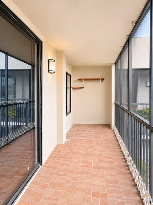 Covered balcony featuring terracotta-style tile flooring, floor-to-ceiling screened enclosures, metal railings, wall-mounted exterior lighting, and built-in wood shelving