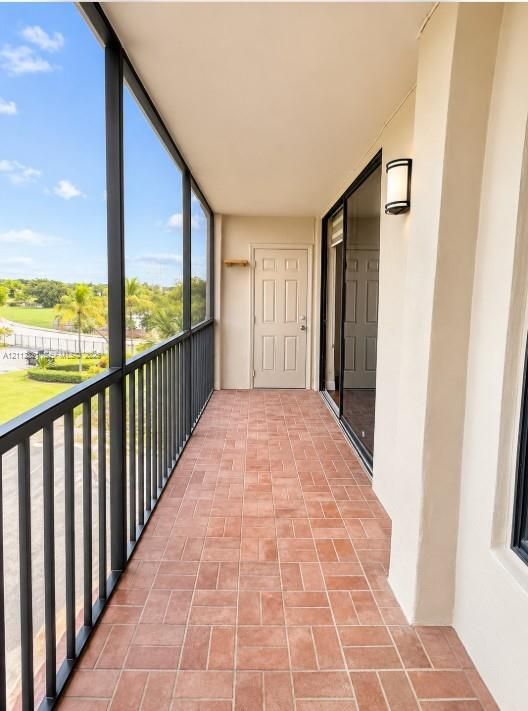 Screened-in balcony featuring terra-cotta tile flooring, black metal railings, a wall-mounted exterior light fixture, and a solid-core entry door