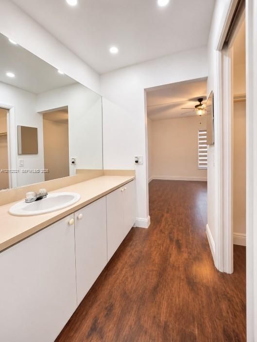 Bathroom vanity featuring white cabinetry, a solid surface countertop, an undermount oval sink, and a full-width wall mirror, complemented by wood-finish flooring