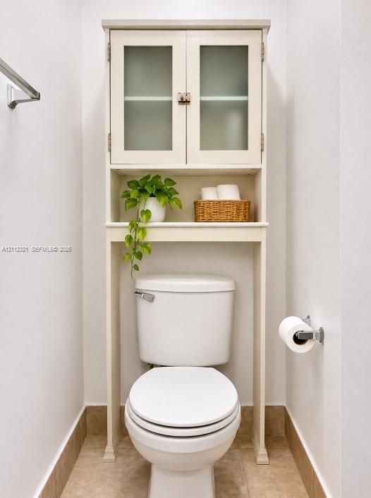 Built-in cabinetry featuring glass-panel doors and open shelving, paired with a ceramic toilet, stainless steel towel bar, and metallic toilet paper holder