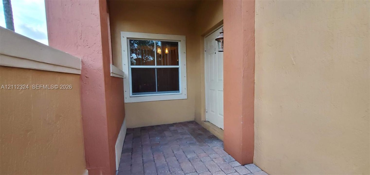 Covered entry featuring paver flooring, stucco exterior walls, and a single-pane window with trim