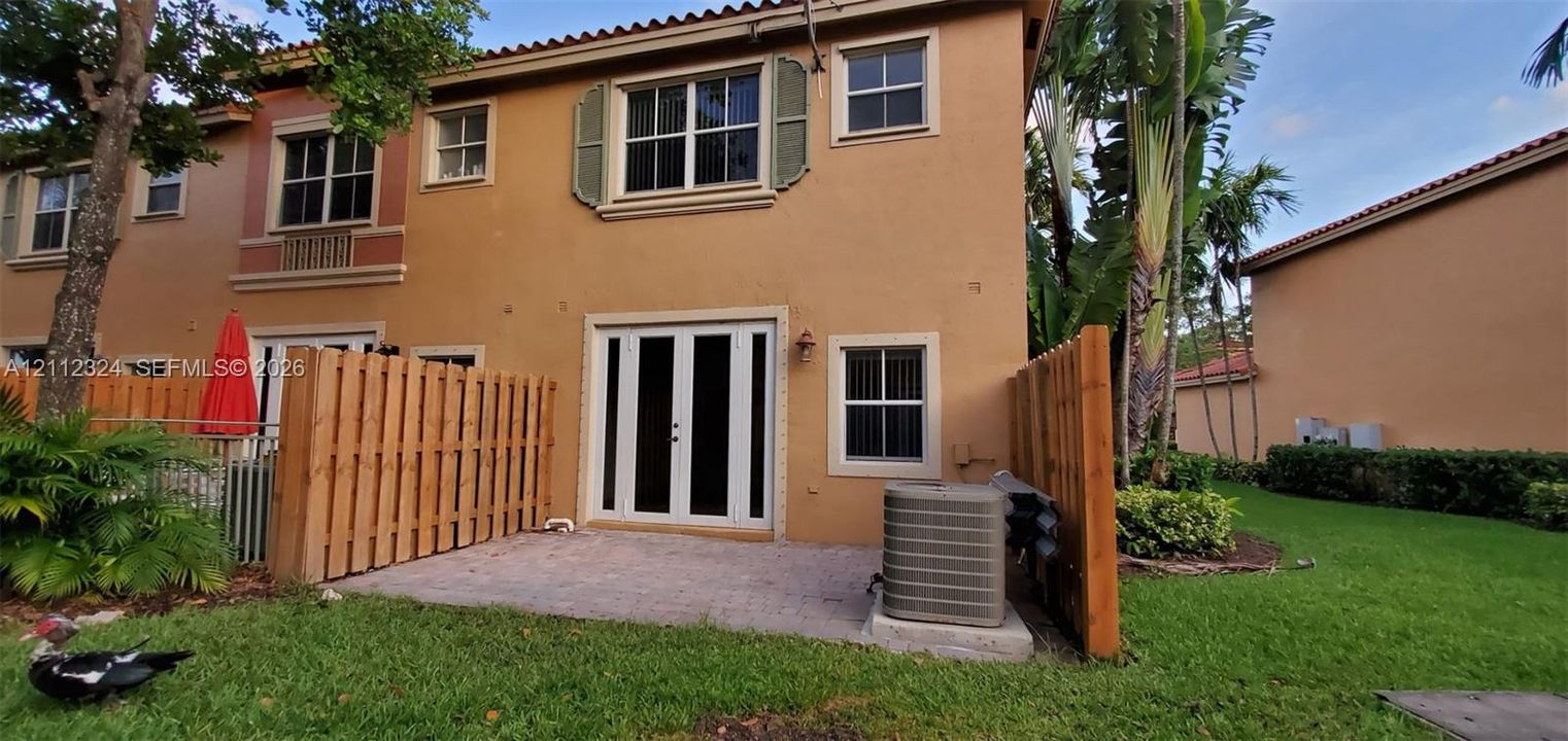 Stucco exterior featuring dual-pane windows, decorative shutters, a paved rear patio, and wood privacy fencing