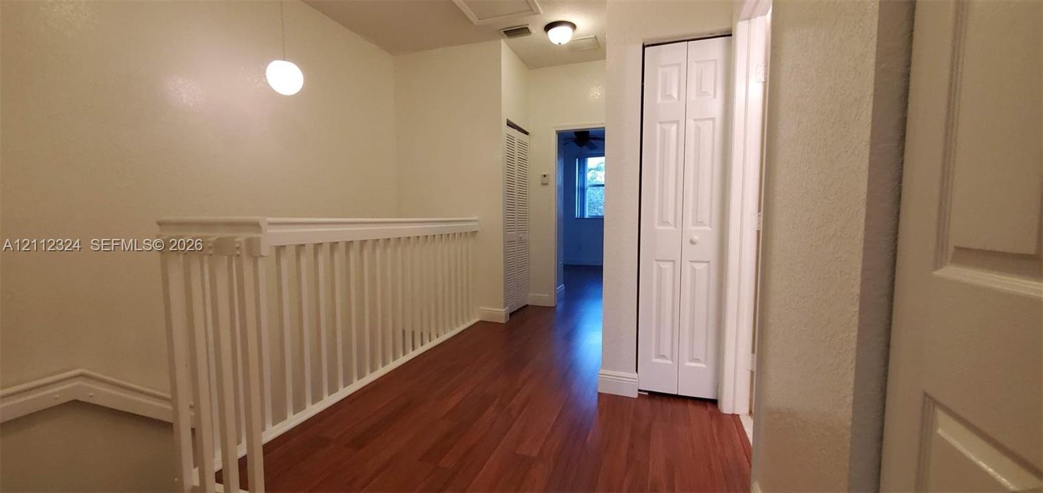 Hallway featuring wood-finish flooring, white spindle railing, flush-mount lighting, and dual bifold closet doors