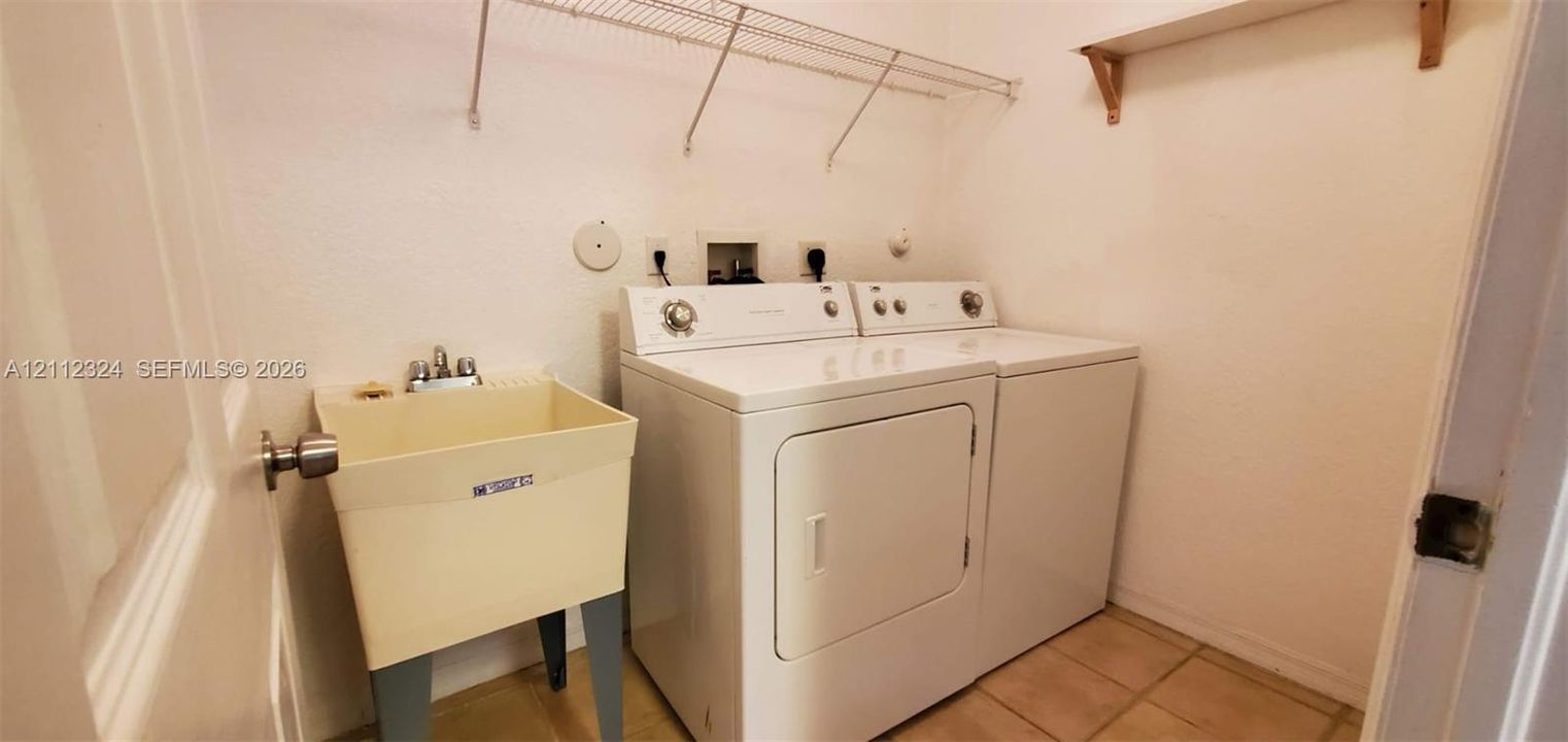 Laundry area featuring a utility sink, metal wall-mounted shelving, and tile flooring