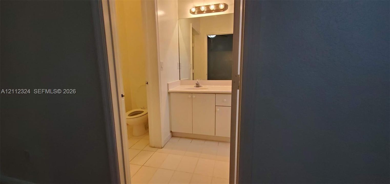 Bathroom featuring a white vanity cabinet, a solid surface countertop with an integrated sink, a large wall-mounted mirror, and tile flooring