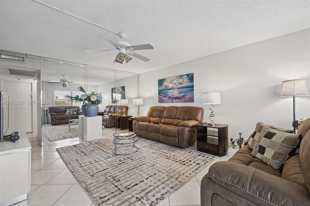 Living area featuring neutral tile flooring, mirrored wall paneling, and a ceiling-mounted light fixture with fan
