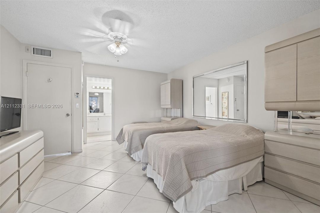 Neutral-toned space featuring large-format diagonal tile flooring, custom built-in light-wood cabinetry, a wall-mounted glass mirror, and a central ceiling fan with integrated lighting