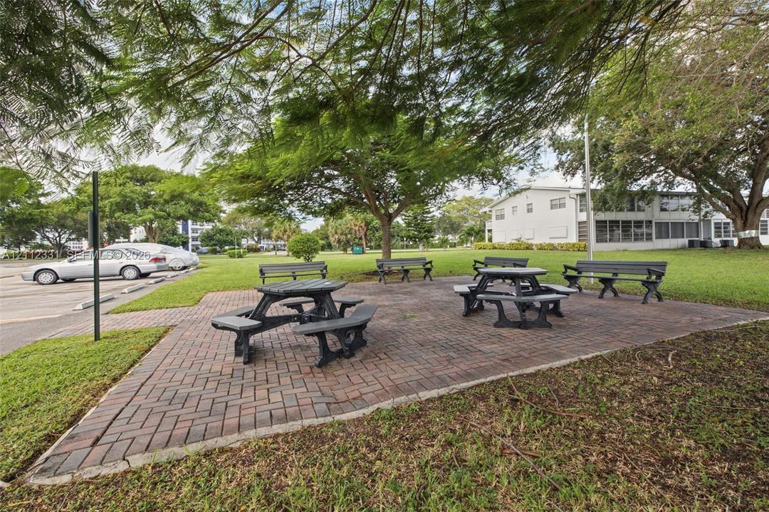 Outdoor common area featuring a brick-paver patio, permanent benches, and mature shade trees