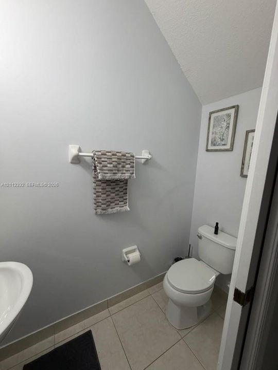 Powder room featuring light-toned neutral wall paint, white ceramic toilet, wall-mounted towel bar, and tile flooring