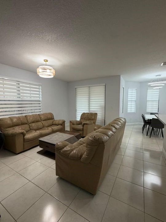 Open-concept interior featuring large-format tile flooring, tiered drum-style pendant lighting, and multiple windows fitted with adjustable horizontal blinds