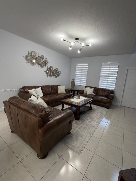 Large-format tile flooring, multi-arm sputnik-style ceiling light fixture, and dual windows equipped with horizontal roller shades