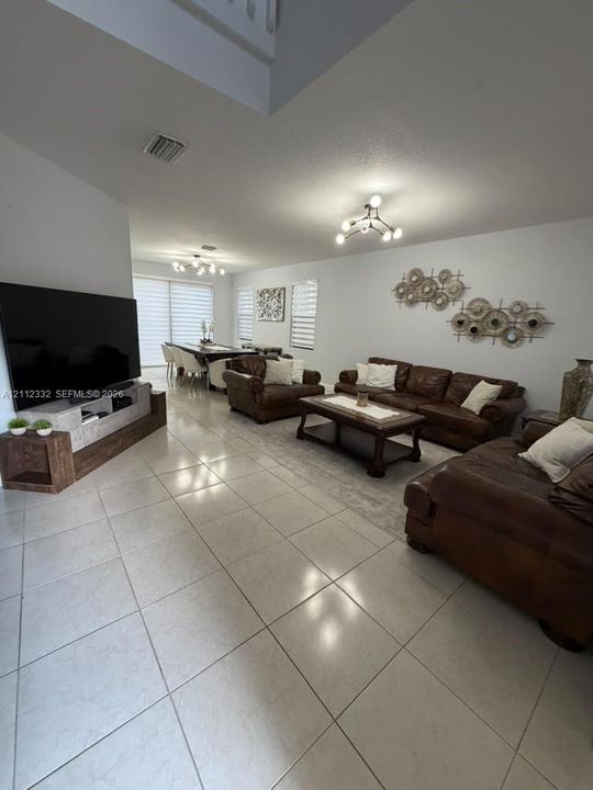 Open-concept interior featuring large-format tile flooring, multi-arm contemporary light fixtures, and windows finished with horizontal blinds