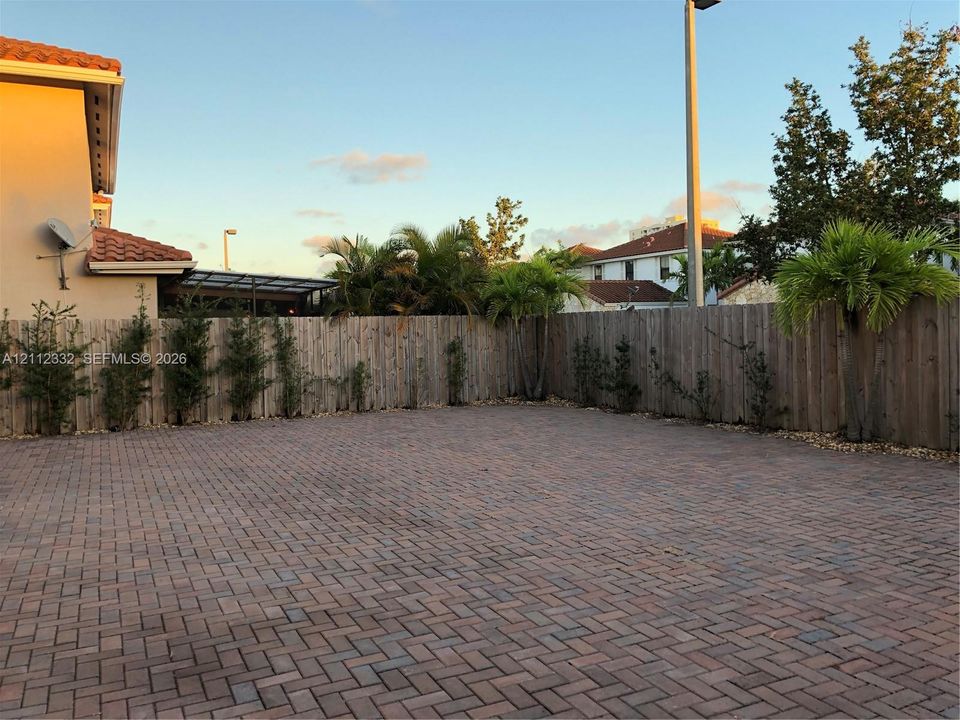 Expansive brick-paver patio area enclosed by a wood privacy fence, accented by mature palm trees and perimeter shrubbery
