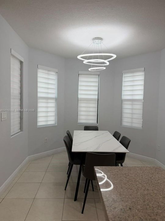 Bay area featuring four rectangular windows with horizontal blinds, large-format tile flooring, and a multi-tiered circular LED pendant light fixture