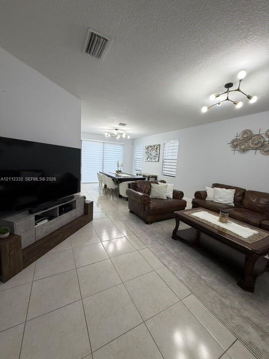 Open-concept interior featuring large-format tile flooring, modern multi-arm branched light fixtures, and sliding glass doors with adjustable light-filtering window treatments
