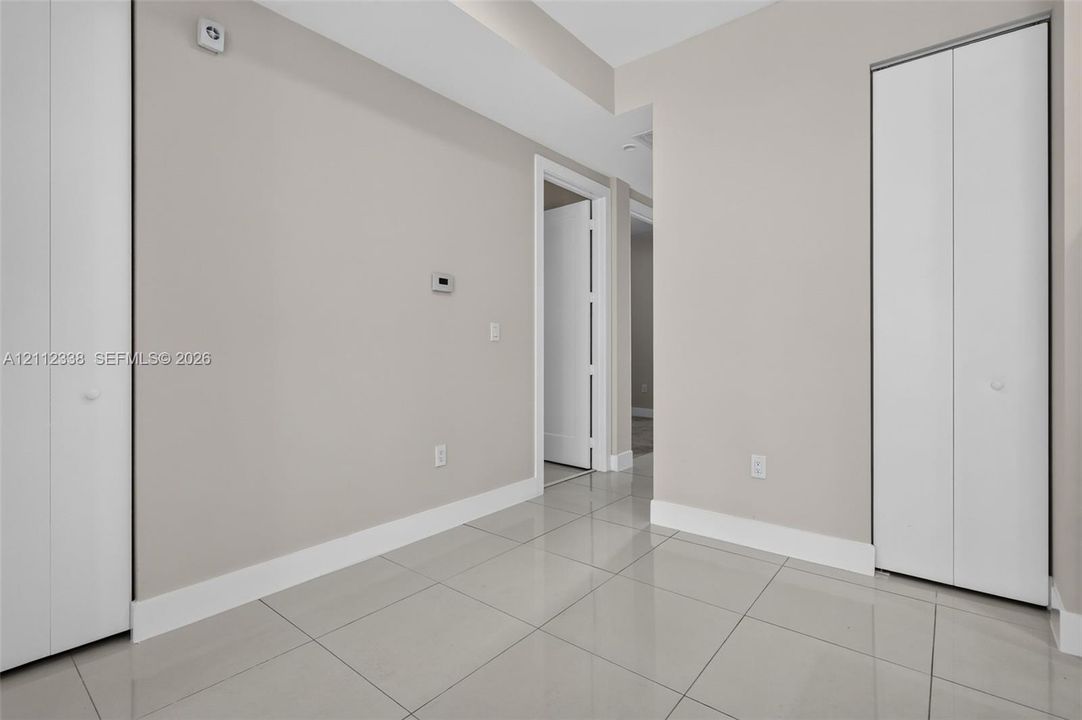 Interior space featuring large-format neutral tile flooring, two sets of white bi-fold closet doors, and smooth wall finishes