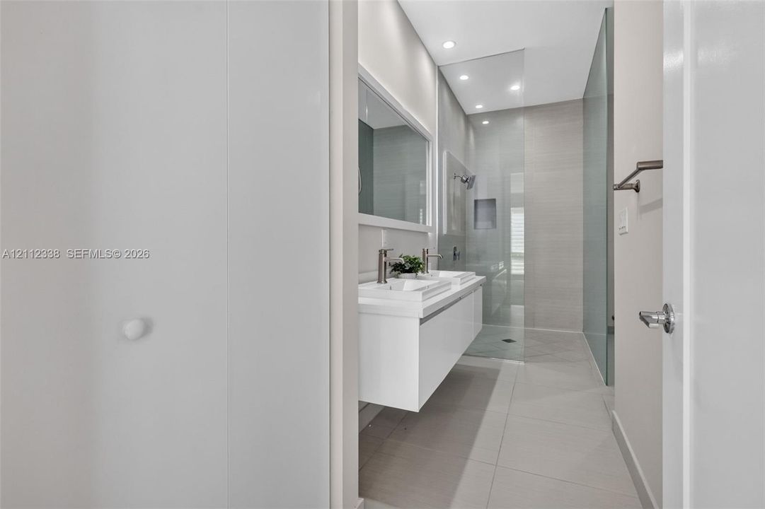 Modern floating dual vanity with integrated sinks, recessed lighting, large-format tile flooring, and a walk-in shower enclosed by a seamless glass panel