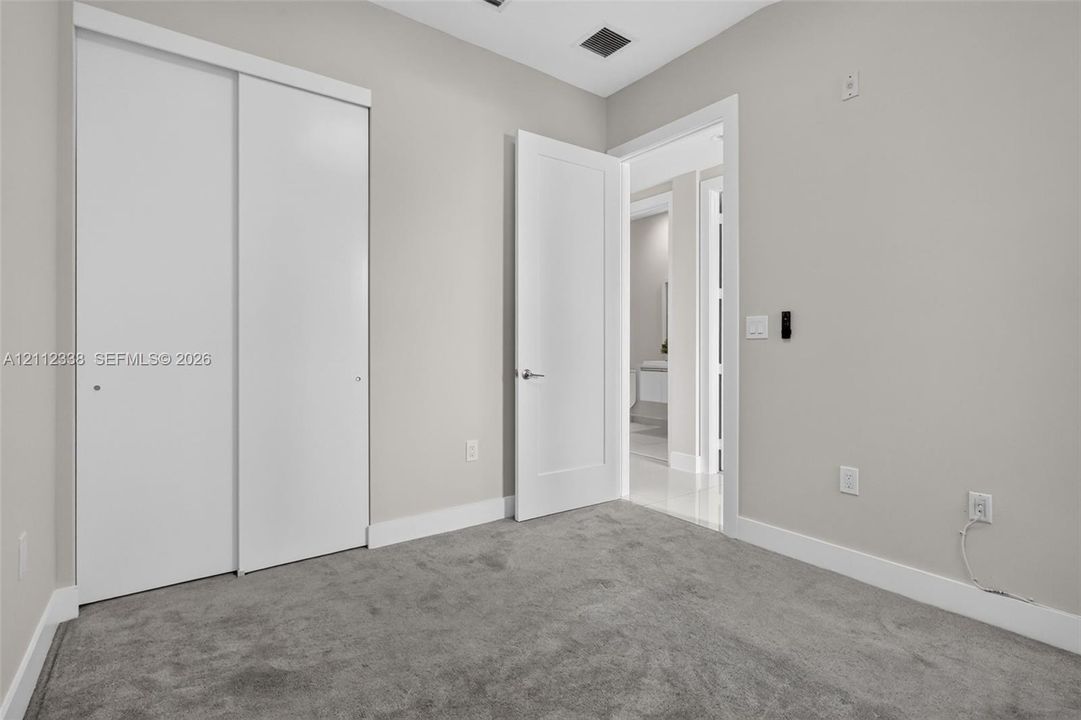 Room featuring neutral wall tones, plush wall-to-wall carpeting, white sliding closet doors, and a solid-core hinged interior door