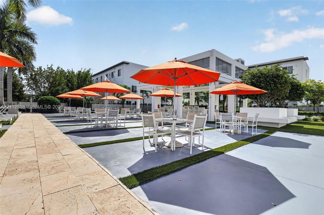 Outdoor recreation area featuring a paved stone walkway, hardscaped patio surface with synthetic grass inlays, and an open-air covered pavilion