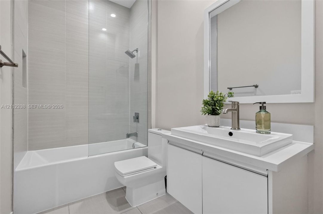 Full bathroom featuring a white vanity with a rectangular vessel sink, solid surface countertop, glass shower panel, and light-toned wall tile