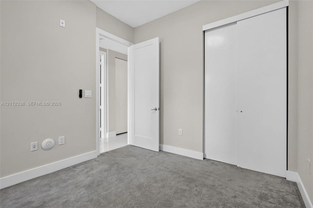 Interior space featuring plush neutral carpeting, smooth-finish walls, a solid-core swing door with brushed metal hardware, and a sliding-panel closet with white finishes
