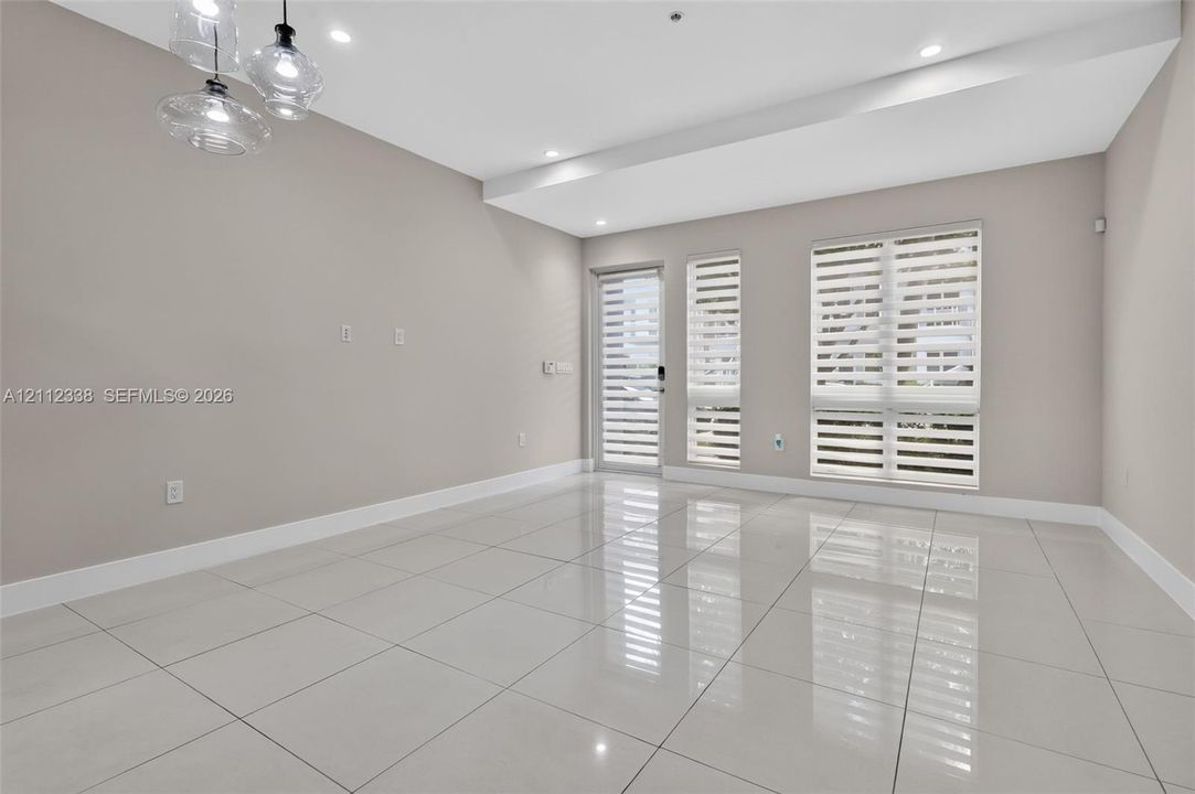Large-format polished tile flooring, recessed ceiling lighting, multi-pendant glass light fixture, and windows featuring dual-layer horizontal blinds