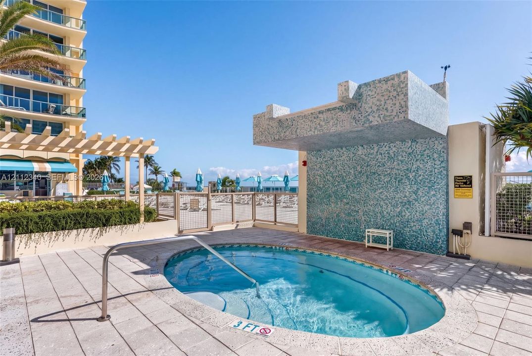 In-ground hot tub featuring a tiled surround, integrated stairs, stainless steel handrail, and a decorative mosaic tile water feature