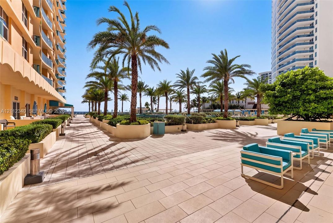 Outdoor terrace featuring expansive stone paving, tiered concrete planters, mature palm trees, and manicured shrubbery