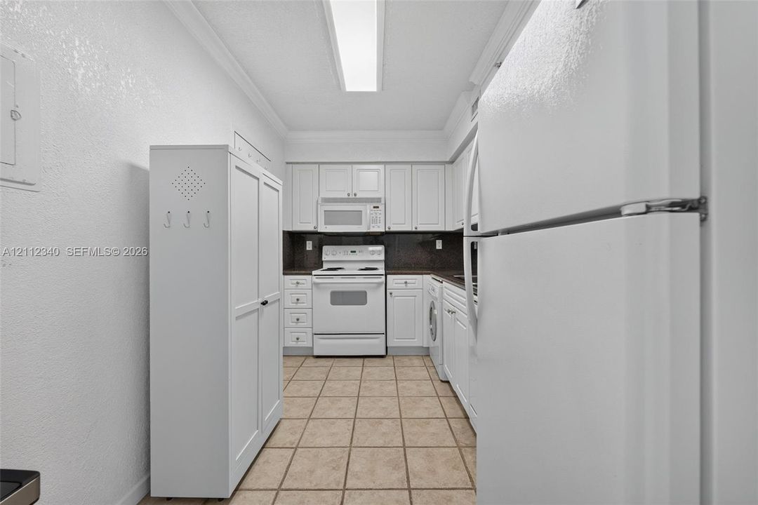 Kitchen featuring white cabinetry, tile flooring, integrated white appliances, and linear ceiling lighting