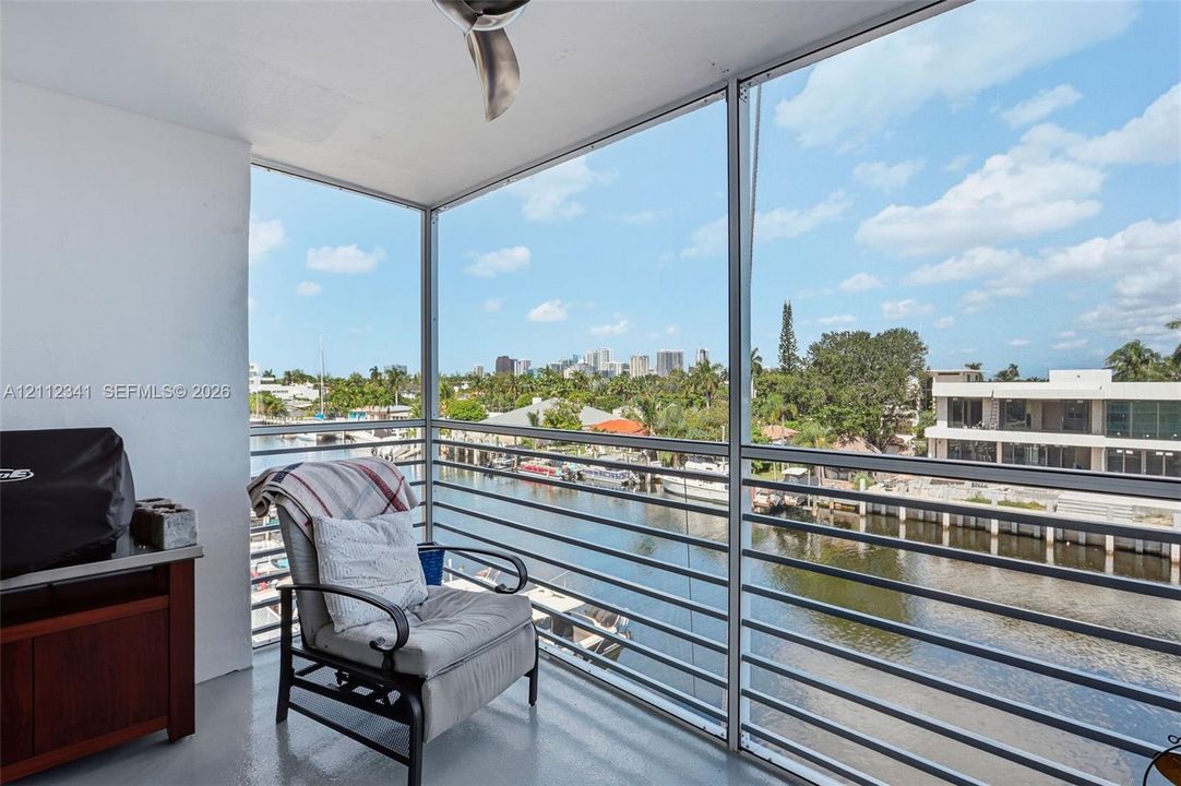 Screened balcony featuring horizontal metal railing and a ceiling-mounted fan, overlooking a canal and urban skyline