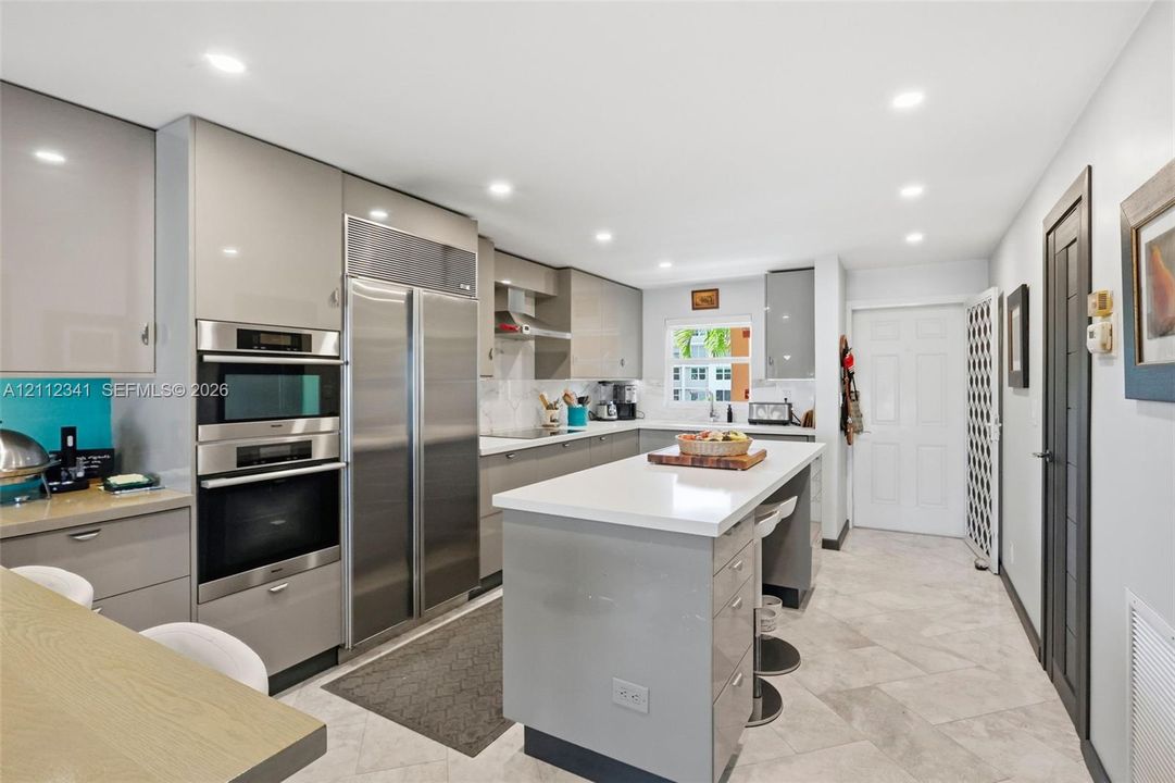 Kitchen featuring high-gloss cabinetry, stone countertops, a central island with integrated seating, stainless steel double-wall ovens, and large-format tile flooring