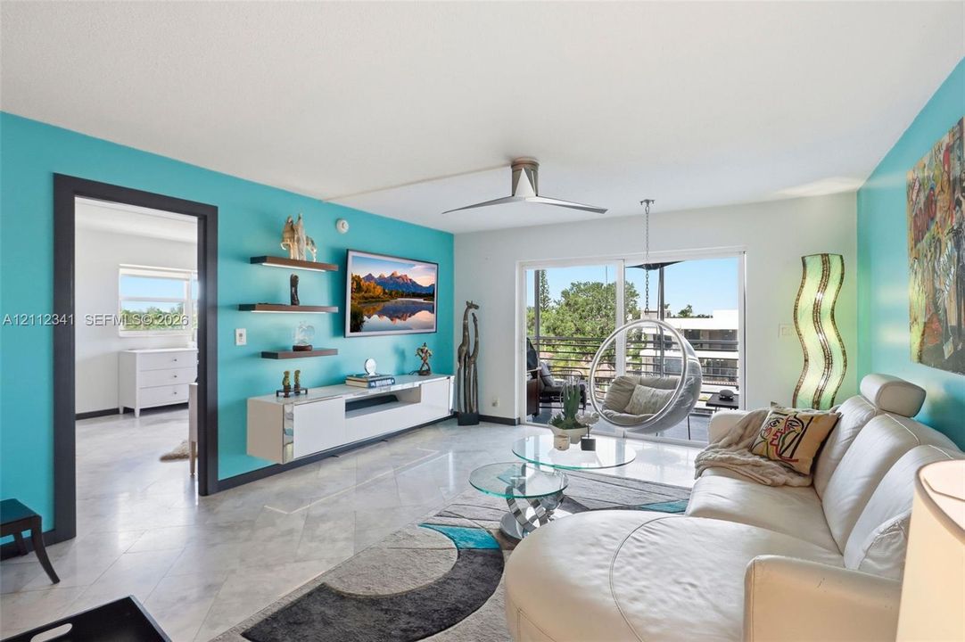 Living area featuring stone-finish flooring, a contemporary ceiling fan, built-in floating cabinetry with illuminated shelving, and sliding glass doors opening to a balcony
