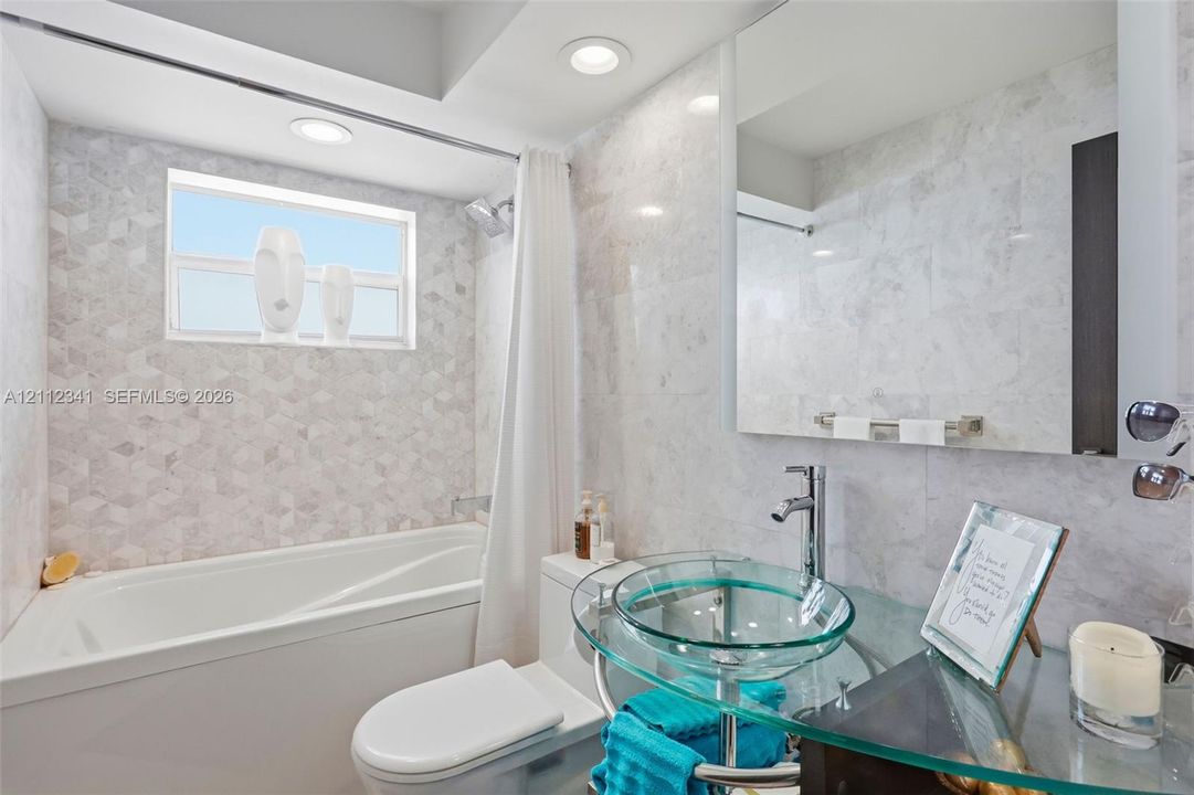 Bathroom featuring full-height decorative stone-patterned wall tile, glass vessel sink, chrome faucet, and recessed lighting