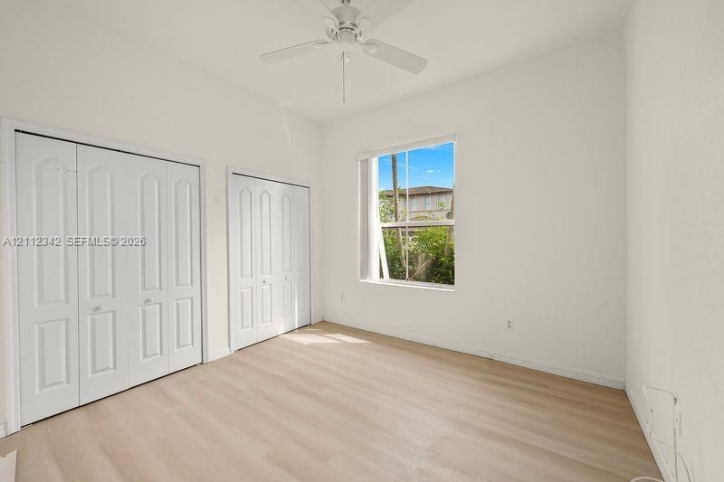 Room featuring wood-finish flooring, dual bi-fold door closets, a single-hung window, and a ceiling fan