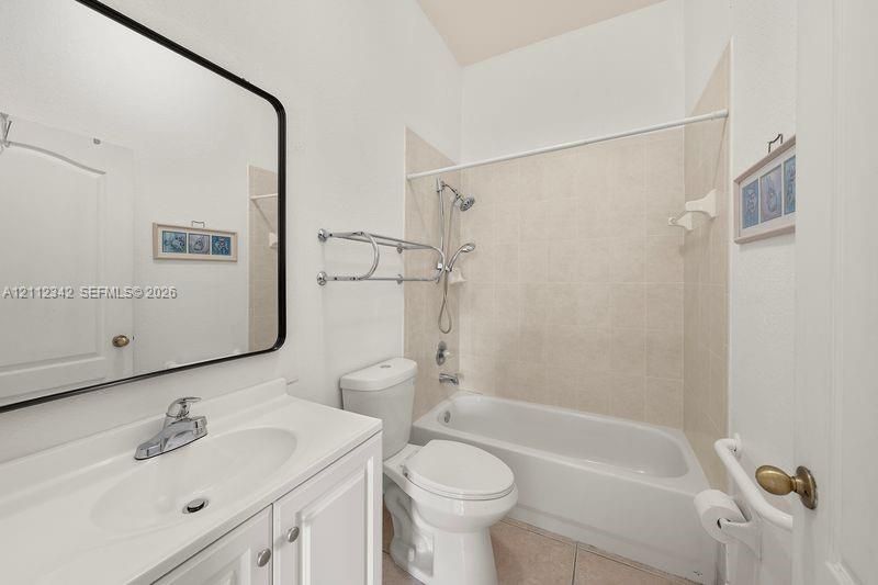 Bathroom featuring a white vanity with integrated basin, polished chrome faucet, black-framed mirror, and a tub-shower combination with ceramic tile surround