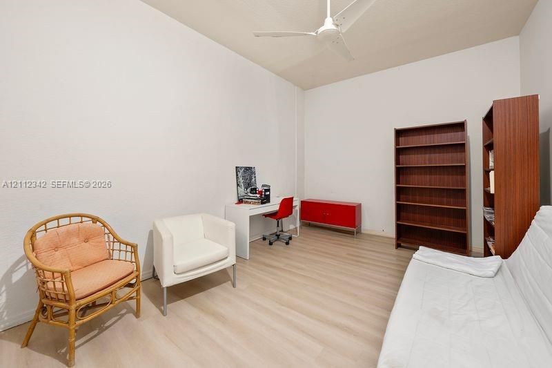 Neutral-toned room featuring wood-finish flooring, high ceilings, and a ceiling fan