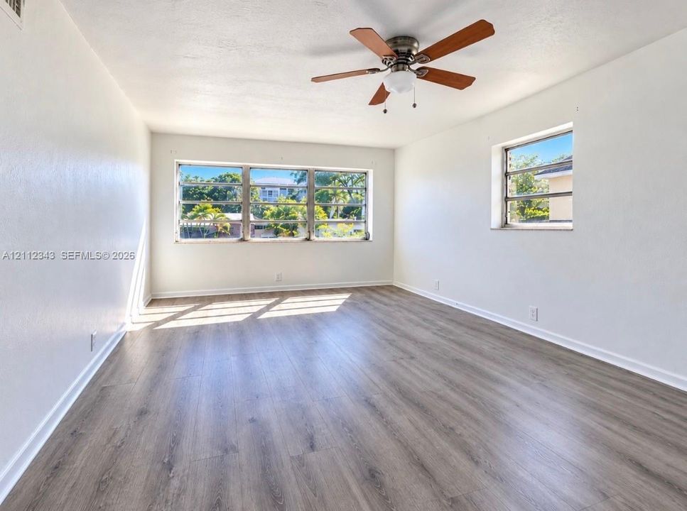 Wood-finish flooring, large multi-pane windows, and a ceiling-mounted fan with integrated lighting