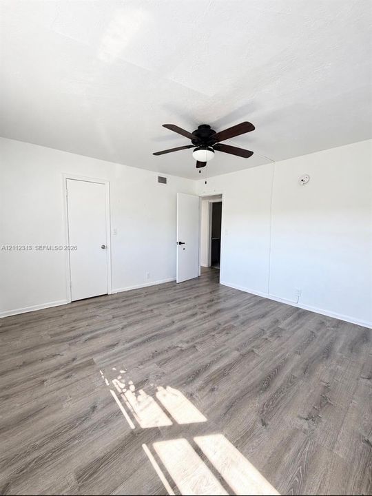 Interior room featuring wood-finish flooring, a multi-blade ceiling fan with integrated lighting, and two doors