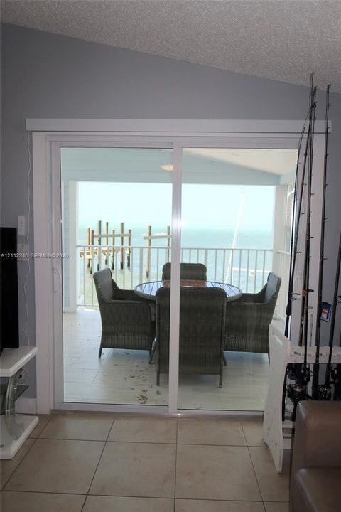 Sliding glass door opening to a covered balcony with a white metal railing, tile flooring, and coastal water backdrop