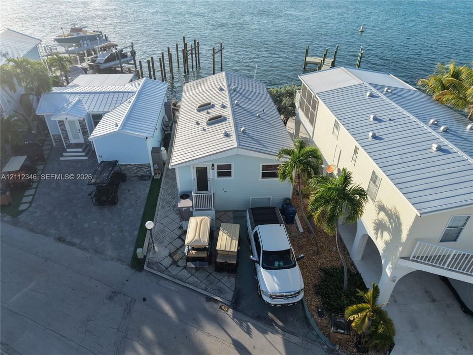 Waterfront property featuring a private boat dock, metal roofing, paved driveway, and palm-lined exterior landscaping