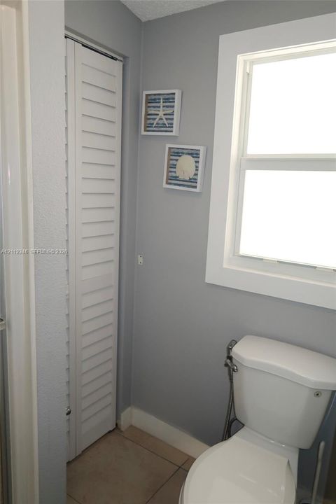 Full-height white louvered door, ceramic tile flooring, and a single-hung window with white casing