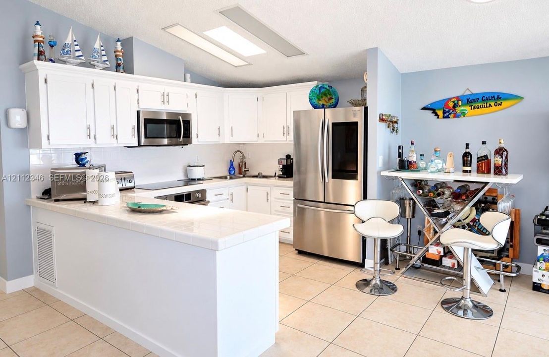 Kitchen featuring white cabinetry, tile countertops, stainless steel appliances, and tile flooring